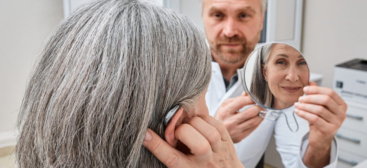 An audiologist holds a mirror up to a patient wearing a hearing aid